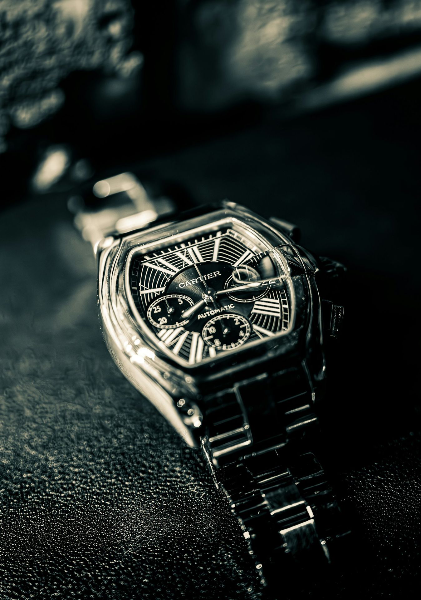 A cartier watch lies on a textured surface.